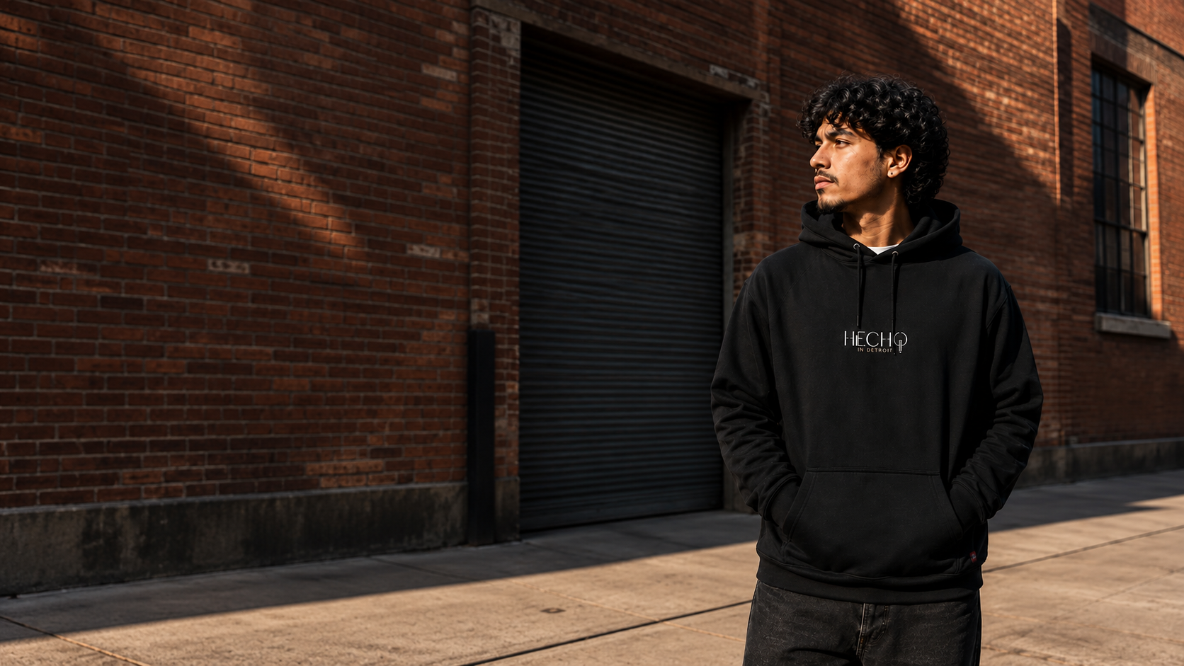 Black Hecho Hoodie against sunlit Detroit brickwork